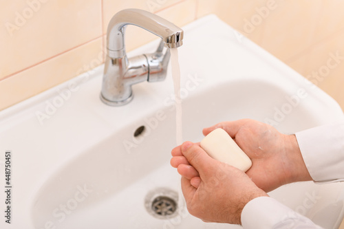 hand washing with soap or gel under running water in the washbasin, cleanliness and hygiene, men's hands dressed in a white shirt