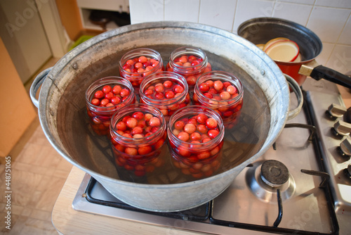 Cherry compote being prepared for winter preservation in a big pot on a stove, where all bacteria is destroyed because of heat.
