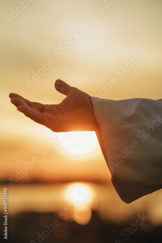 Jesus Christ reaching out his hand at sunset.