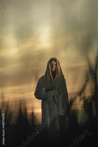 Jesus Christ walks in meadow in white robe at sunset. photo