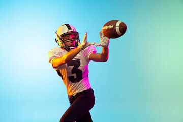 One male American football player training isolated on blue studio background in neon light. Concept of sport, competition