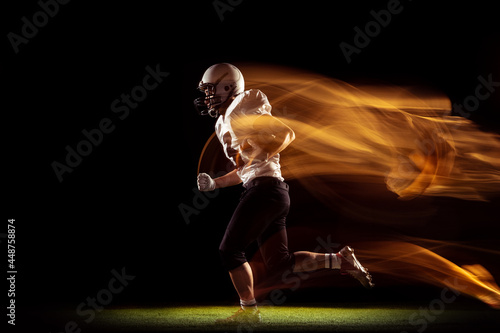 Portrait of young man, American football player training isolated on dark studio background with mixed neon light. Concept of sport, competition and beauty © master1305