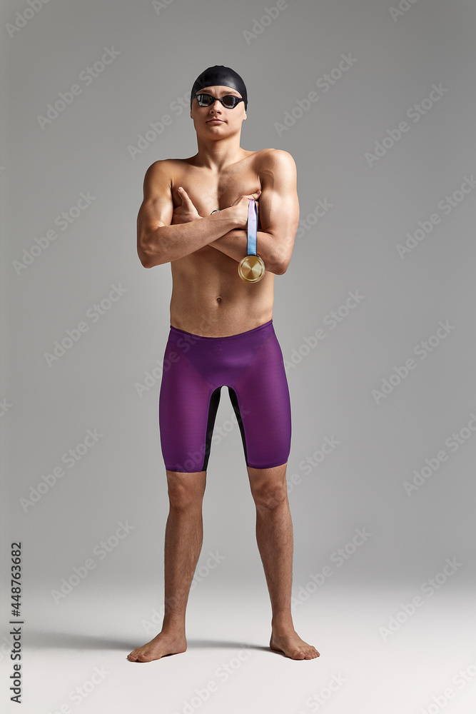 Swimmer with a medal on a gray background rejoices in victory, an athlete in excellent physical shape celebrates a victory clutching a medal in his hand, victory concept, gray background, copy space Swimmer with a medal on a gray background rejoices in victory, an athlete in excellent physical shape celebrates a victory clutching a medal in his hand, victory concept, gray background, copy space