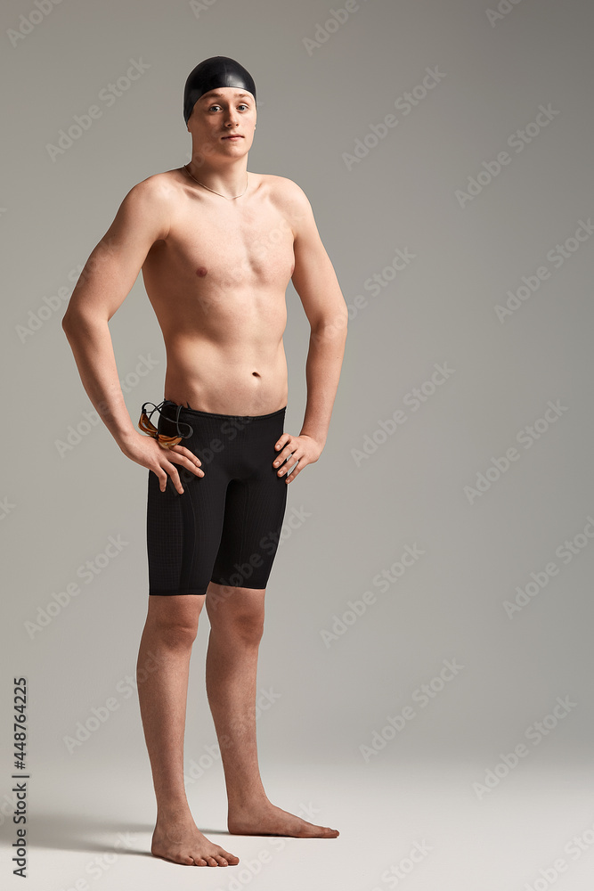 A man swimmer in goggles for swimming in full growth on a gray background, preparing an athlete for a swim, copy space