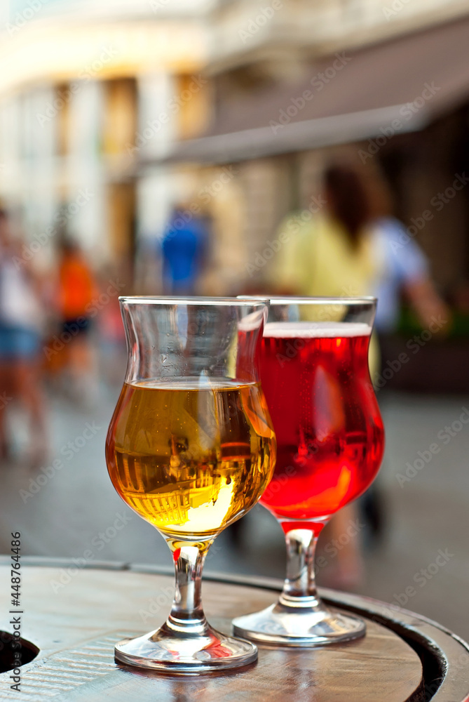 Glass of red and white wine close up. Alcoholic liqueur on a wooden barrel on a background of the city. Blurred people in the background. Glass of red and white wine close up. Alcoholic liqueur on a wooden barrel on a background of the city. Blurred people in the background.