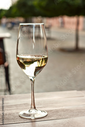 Glass of white wine close up. Alcoholic drink on a wooden table on a background of the city. Transparent wine on the summer terrace of the restaurant.