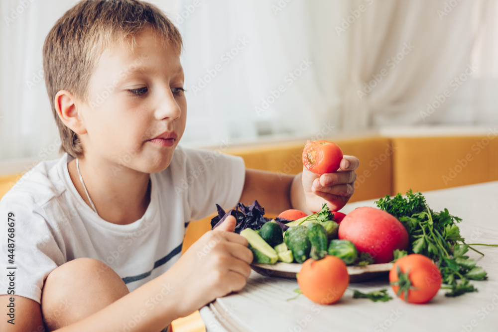 Boy sitting in the kitchen eating healthy vegetables cucumber and tomato Boy sitting in the kitchen eating healthy vegetables cucumber and tomato
