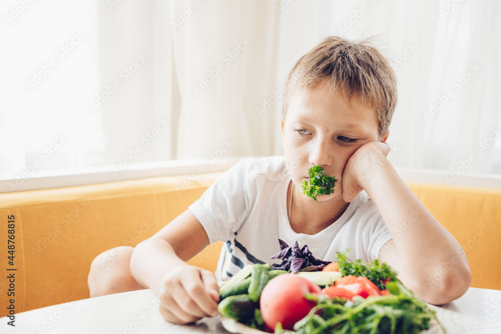 Boy sitting in the kitchen eating healthy vegetables cucumber and tomato Boy sitting in the kitchen eating healthy vegetables cucumber and tomato