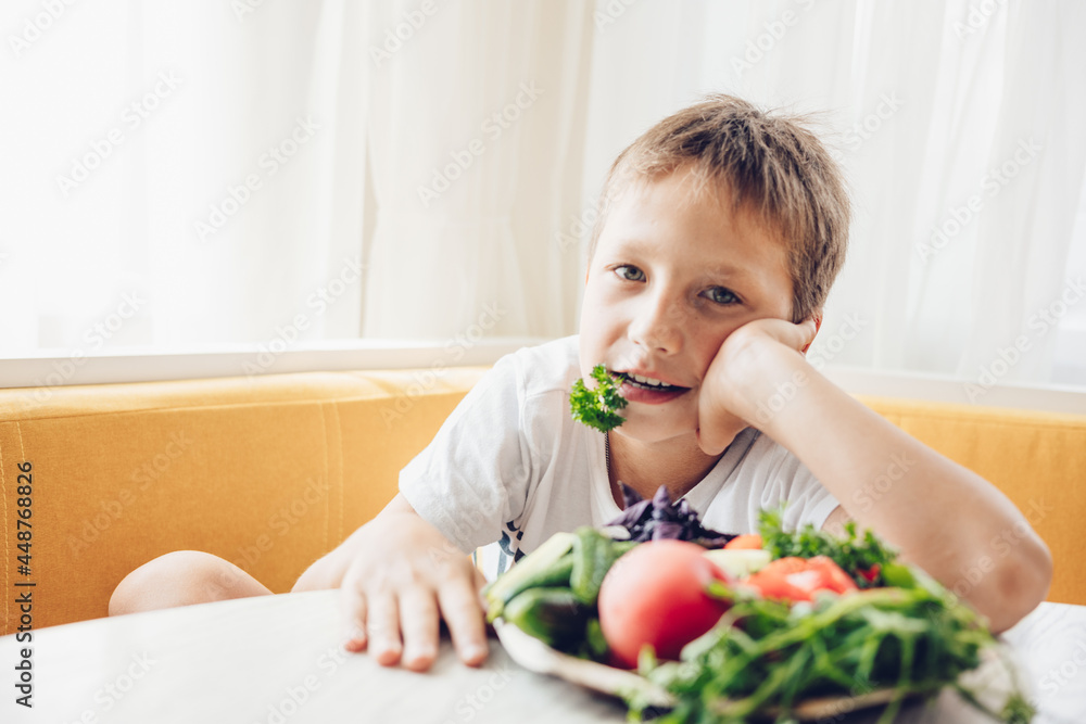 Boy sitting in the kitchen eating healthy vegetables cucumber and tomato Boy sitting in the kitchen eating healthy vegetables cucumber and tomato