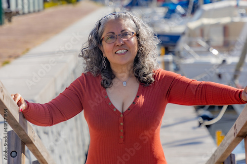 Mature woman smiling at camera wearing casual clothes in the port of Brouwershaven boats in blurred background, sunny day in Schouwen-Duiveland in Zealand, Netherlands. Head shot portrait