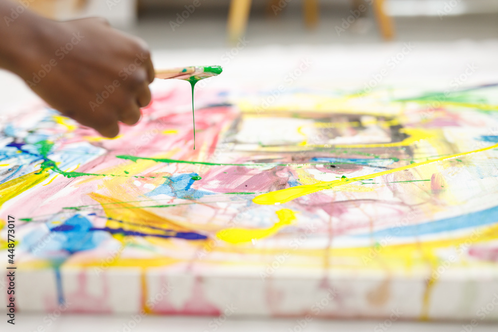 Naklejka premium Close up of african american male painter at work painting on canvas in art studio