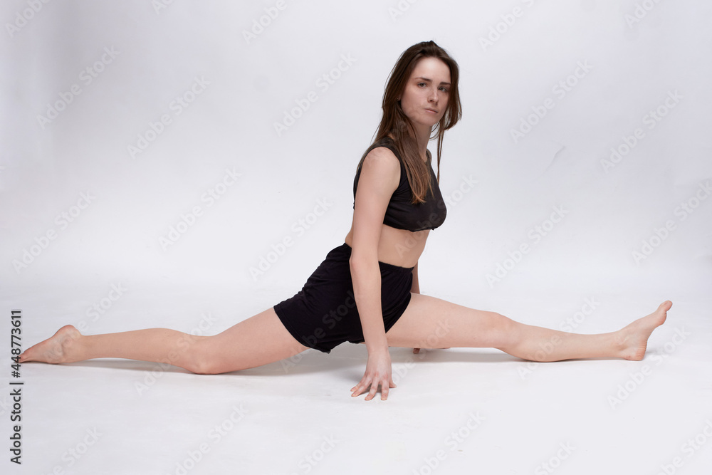 Young slim athletic girl, with long hair, in a black top and shorts, in the studio on a white background, does the splits Young slim athletic girl, with long hair, in a black top and shorts, in the studio on a white background, does the splits