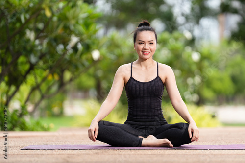 A confident middle-aged Asian woman in sports outfit doing yoga exercise on the yoga mat outdoor in the backyard in the morning. Young woman doing yoga exercise outdoor in the nature public park © EduLife Photos
