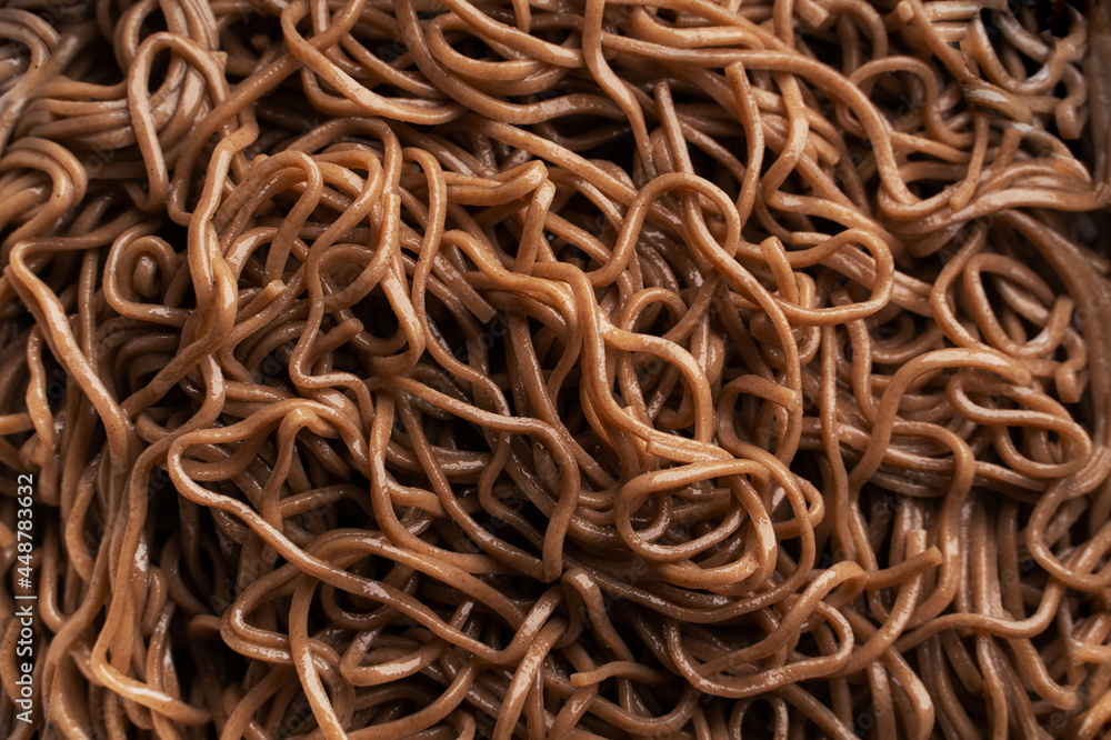 The texture of buckwheat or dark noodles. Brown noodles are visible throughout the frame. An ingredient for making a wok. Asian food. Asian pasta. Cooking food. Strid food. Gluten-free fries. The texture of buckwheat or dark noodles. Brown noodles are visible throughout the frame. An ingredient for making a wok. Asian food. Asian pasta. Cooking food. Strid food. Gluten-free fries.