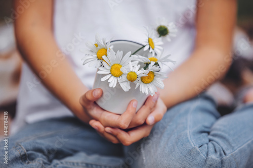 Hands of a child close-up with a bouquet of daisies in a mug