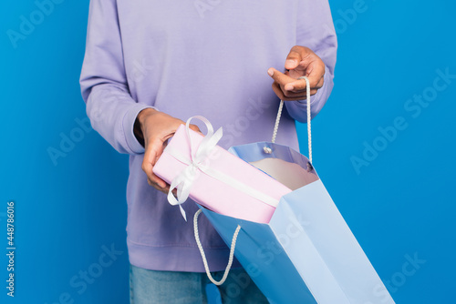cropped view of african american man with paper bag and gift box isolated on blue