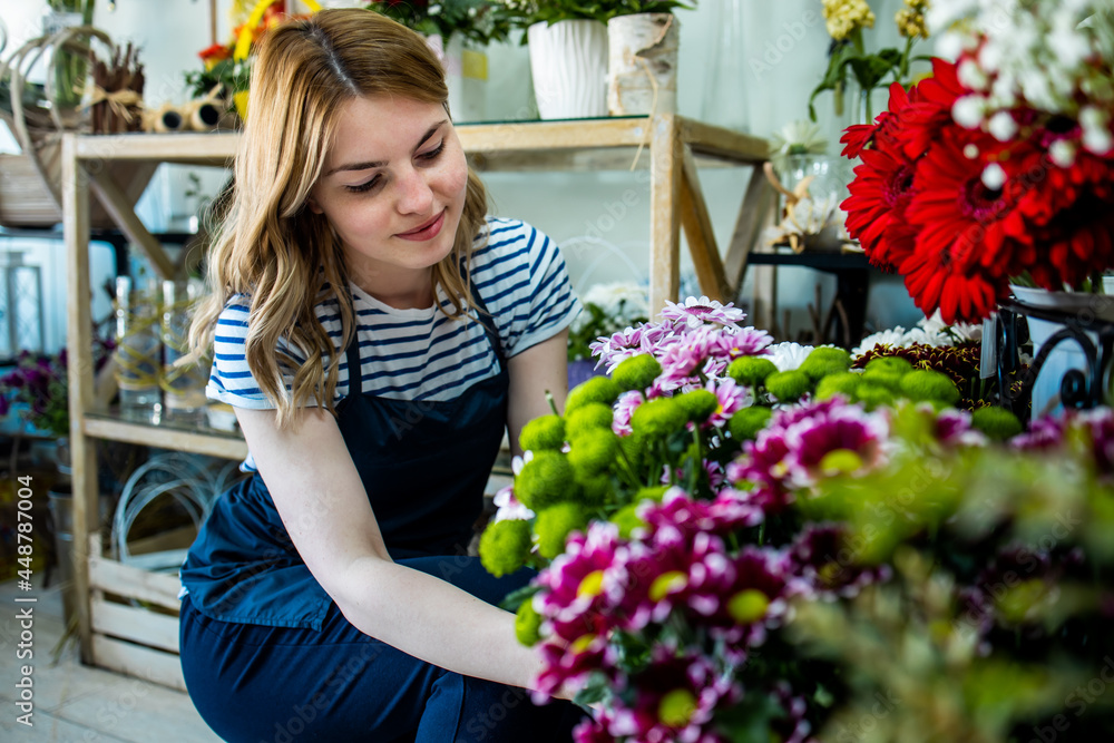 Young adult woman working in city street flower shop.She arranging flowers inside of shop.Small business concept.