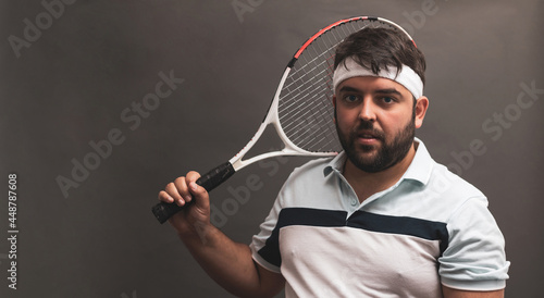  a fat man posing with a tennis racket on a gray background. ©  Yistocking