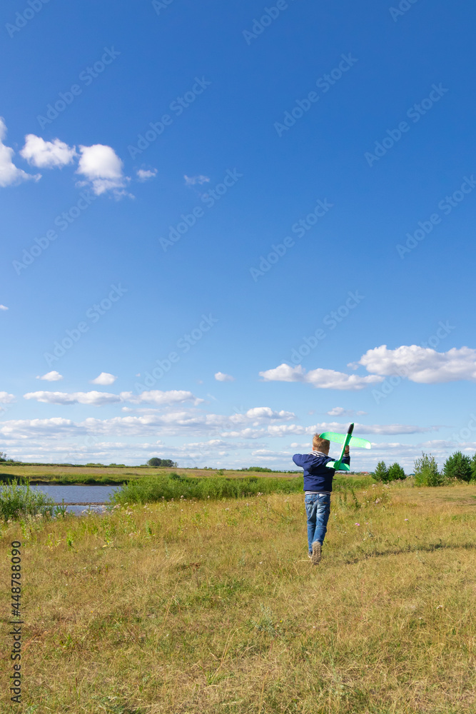 A six-year-old preschooler boy in a blue jacket launches a toy plane in a field against a blue sky with clouds on a summer day. The bright sun is shining. Scenery A six-year-old preschooler boy in a blue jacket launches a toy plane in a field against a blue sky with clouds on a summer day. The bright sun is shining. Scenery