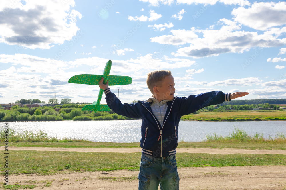 A six-year-old preschooler boy in a blue jacket launches a toy plane in a field against a blue sky with clouds on a summer day. The bright sun is shining. Scenery A six-year-old preschooler boy in a blue jacket launches a toy plane in a field against a blue sky with clouds on a summer day. The bright sun is shining. Scenery