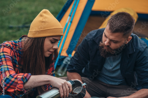 Couple of campers drinking coffee from a metal cup and thermos