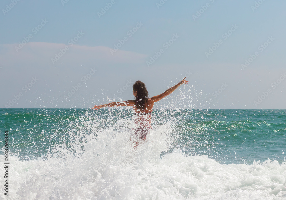 A beautiful girl enjoying the waves of the ocean. Splashes, lots of drops.