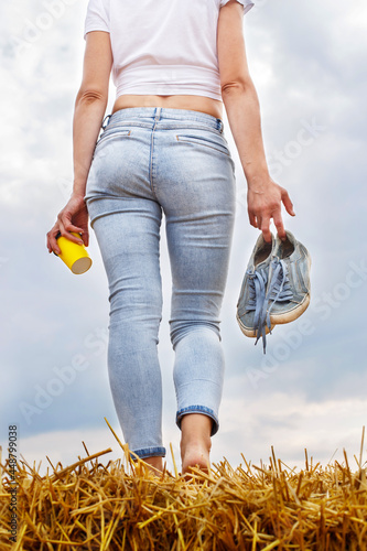 barefoot girl with sneakers and cardboard cup with coffee in hand stand in the agricultural field photo