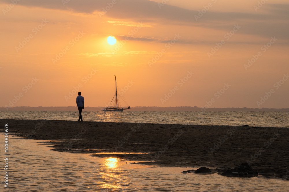 Silhouette of a man walking along the beach at sunset.	
