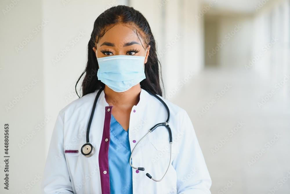 Portrait of african american female doctor wearing mask standing in hospital corridor. medicine, health and healthcare services during coronavirus covid 19 pandemic. Portrait of african american female doctor wearing mask standing in hospital corridor. medicine, health and healthcare services during coronavirus covid 19 pandemic.