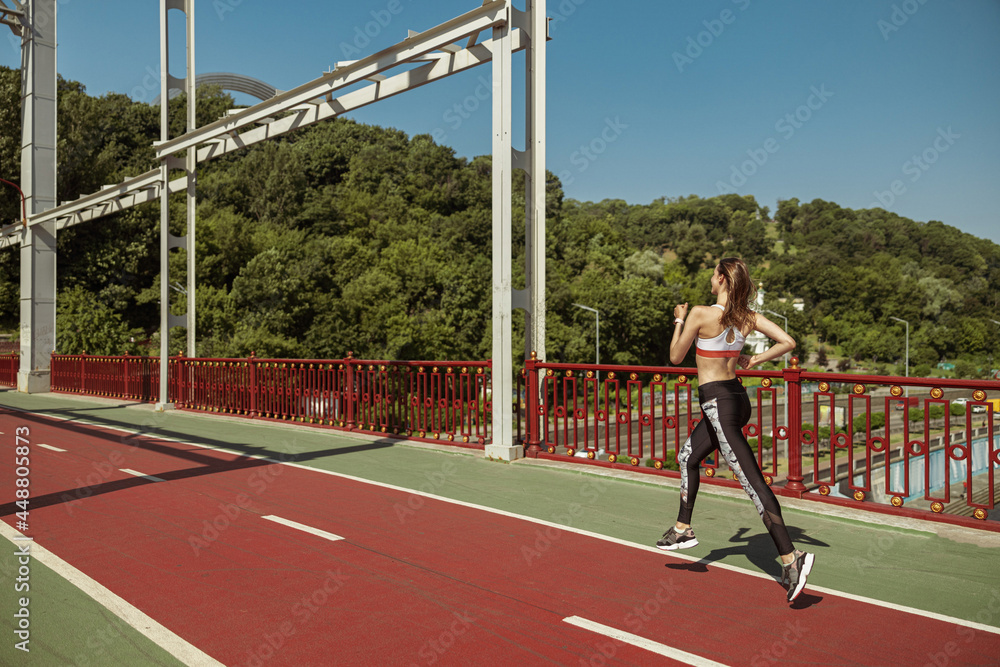 Obraz premium Sportswoman with flying hair runs along footbridge on sunny day