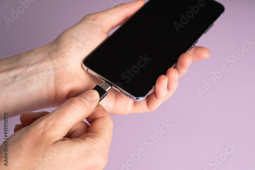 Mobile smart phones charging. Woman hands plugging a charger in a smart phone on violet background