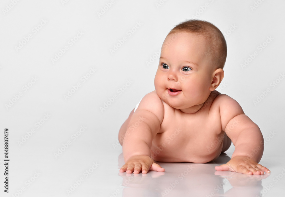 Happy portrait Six month old baby girl in a diaper lying and looking with interest to the side on a white background Happy portrait Six month old baby girl in a diaper lying and looking with interest to the side on a white background