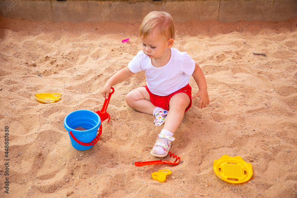 Adorable toddler girl playing with sand on sandbox in playground Adorable toddler girl playing with sand on sandbox in playground