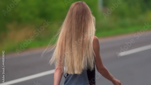 A young blonde girl walks along the highway in a cloudy weather