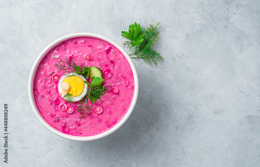 A portion of beetroot soup with egg, dill, parsley and cucumber on a gray background. Top view, copy space. A portion of beetroot soup with egg, dill, parsley and cucumber on a gray background. Top view, copy space.
