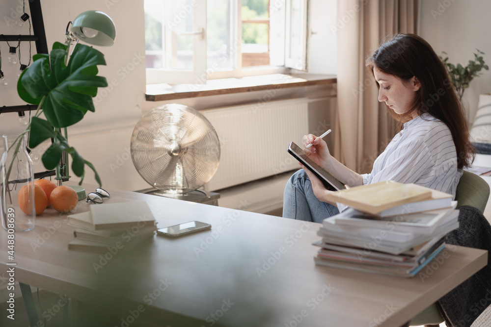 Young beautiful female student with digital tablet studying working at home at the desk Young beautiful female student with digital tablet studying working at home at the desk