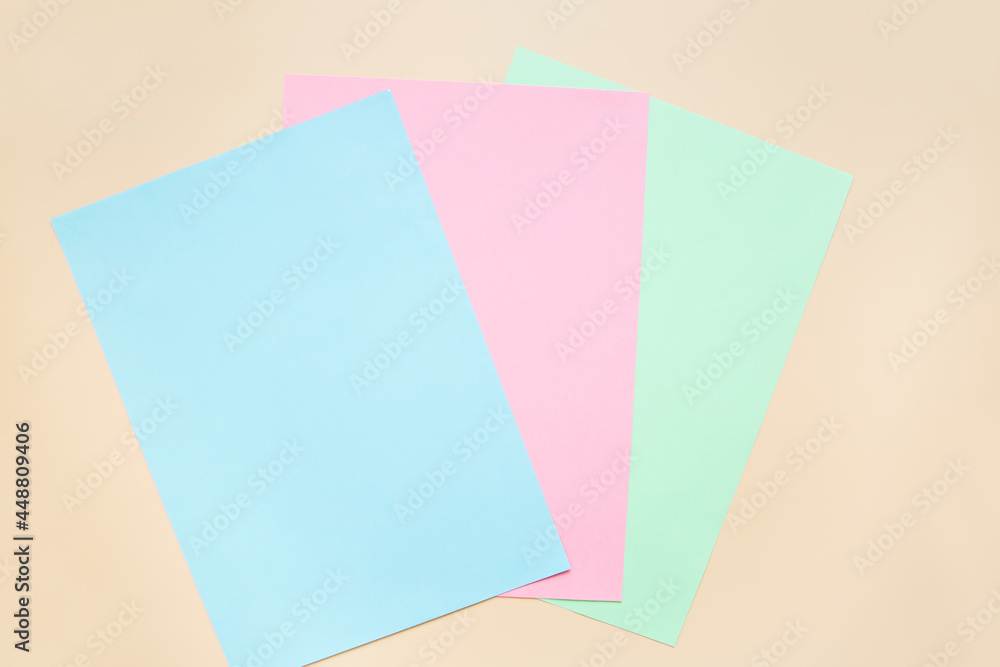 Blank sheets of blue, pink and green colored paper on a beige background. Layout, copy space. Blank sheets of blue, pink and green colored paper on a beige background. Layout, copy space.