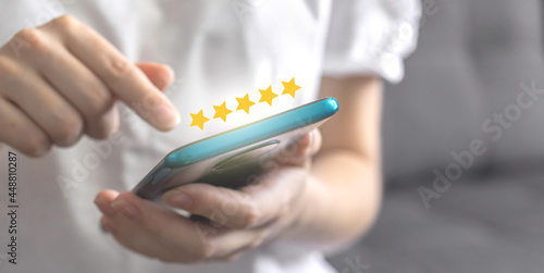 Woman using smartphone for giving the gold five star rating, review the sercive, feedback concept, hand with mobile phone and best score icon, banner photo