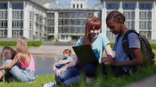 Diverse schoolchildren enjoying break on green lawn using laptop © TommyStockProject