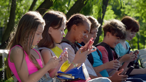 Side view of diverse teenager children using cellphone sitting on bench in park © TommyStockProject