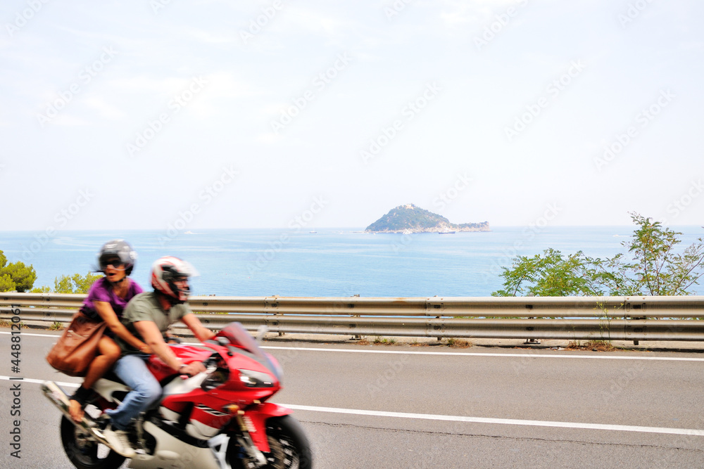 Obraz premium A road along the seashore. Paved road. A man and a woman are riding on a motorcycle. The road along the sea from Italy to France. Cote d'Azur.