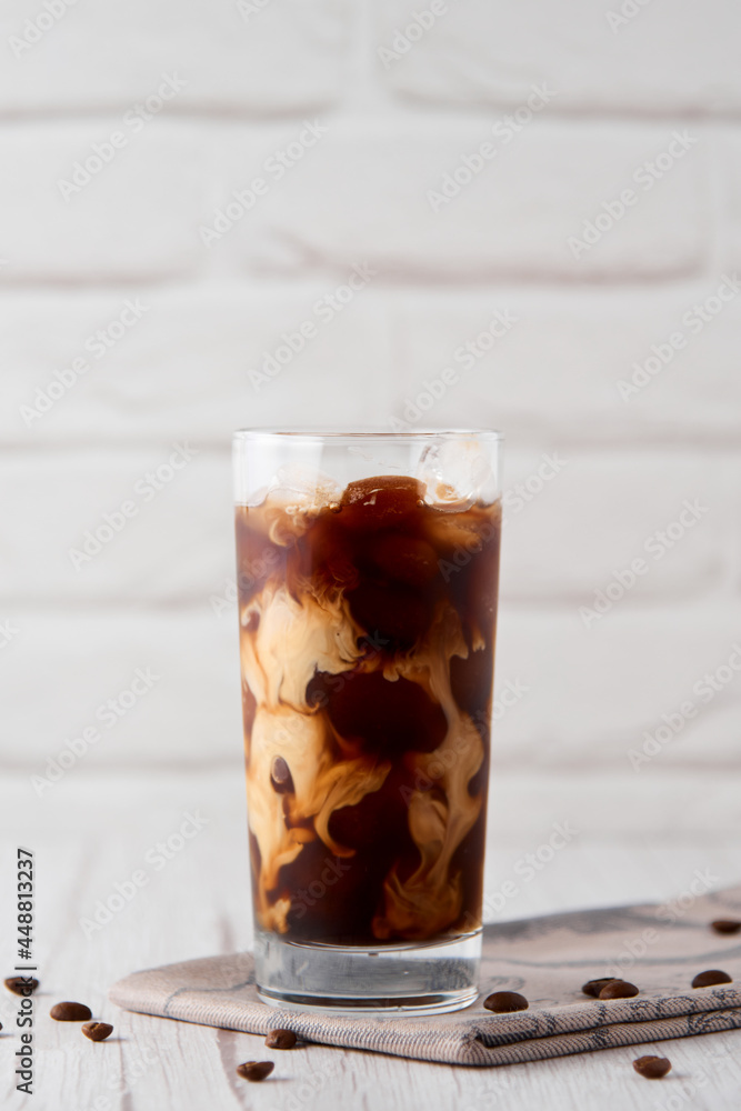 Iced coffee in a tall glass with cream on a white wood background. Cold tasty summer refreshment beverage concept. Selective focus, copyspace. Iced coffee in a tall glass with cream on a white wood background. Cold tasty summer refreshment beverage concept. Selective focus, copyspace.