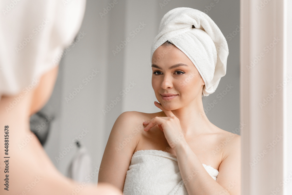 Caucasian white woman with clean young clear skin in spa bath towel looking at the mirror. Beauty treatment, body and hair care. Girl after taking bath shower at home Caucasian white woman with clean young clear skin in spa bath towel looking at the mirror. Beauty treatment, body and hair care. Girl after taking bath shower at home