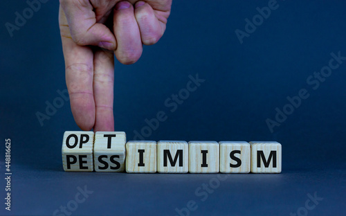 Pessimism or optimism symbol. Businessman turns cubes and changes the word 'pessimism' to 'optimism'. Beautiful grey table, grey background. Business, optimism or pessimism concept. Copy space.