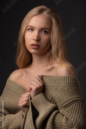 Portrait of a young attractive girl with long curly hair in a warm jacket. The blonde. Black background.