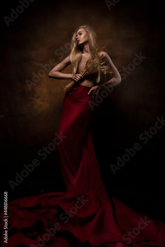 A girl with loose hair on a dark background with wheat in her hands. Artistic photo. The concept of youth, beauty and health. Mysticism, science fiction, fairy tale.