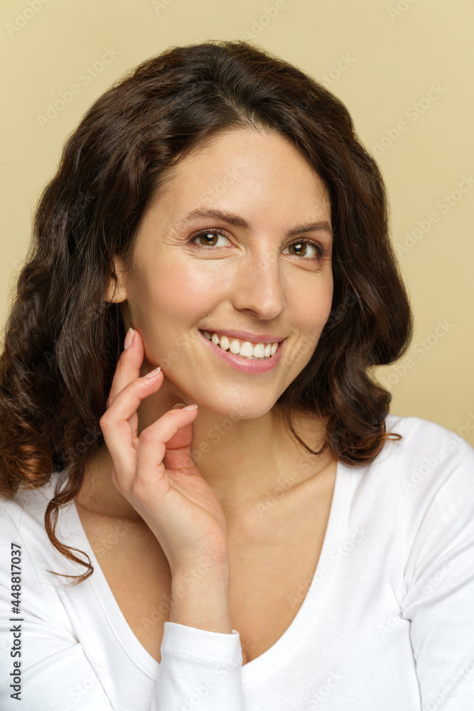 Portrait of millennial woman with natural makeup, perfect smooth skin and toothy smile over beige background. Relaxed young female with curly back hair in white blouse. Beauty and skincare concept Portrait of millennial woman with natural makeup, perfect smooth skin and toothy smile over beige background. Relaxed young female with curly back hair in white blouse. Beauty and skincare concept