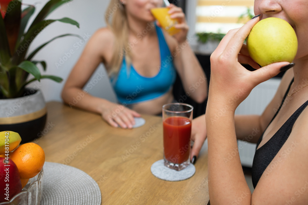 A woman bites the first bite into an apple. The girl in the background is drinking orange juice. A woman bites the first bite into an apple. The girl in the background is drinking orange juice.