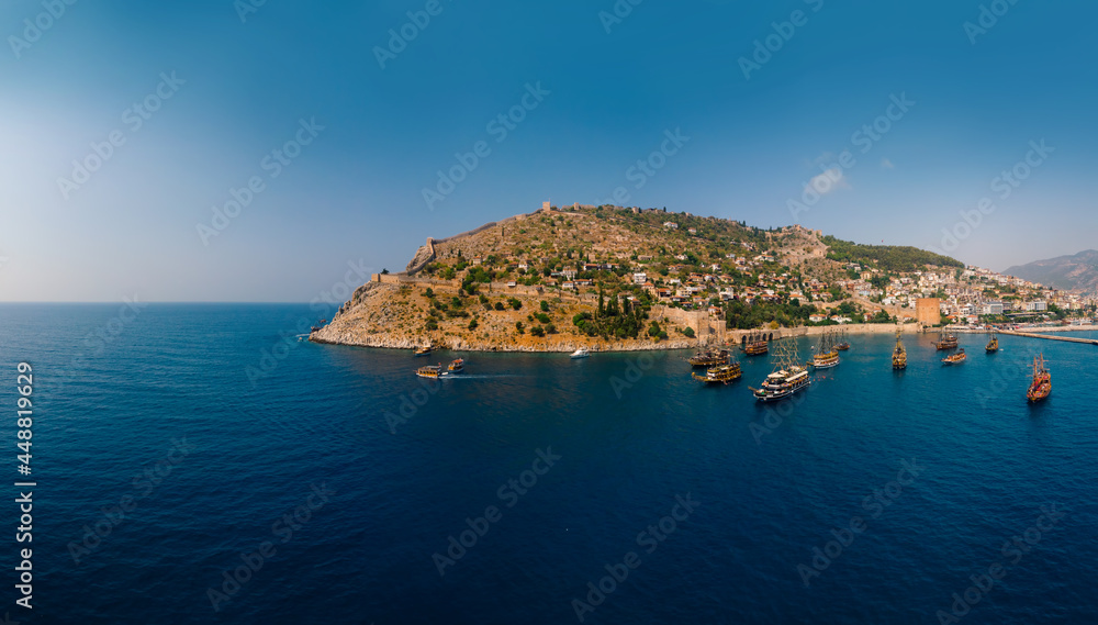 Aerial wide panoramic view of Alanya in southern coast of Turkey, Summer morning day. Travel and vacation. Kalesi Castle. Ships and boats in the mediterranean. Kızılkule bay. lighthouse and pier