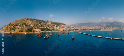 Fototapeta Naklejka Na Ścianę i Meble -  Aerial wide panoramic view of Alanya in southern coast of Turkey, Summer morning day. Travel and vacation. Kalesi Castle. Ships and boats. Show program and entertainment for tourists, swimming